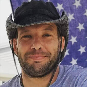 Man in cowboy hat smiles in front of an American flag.