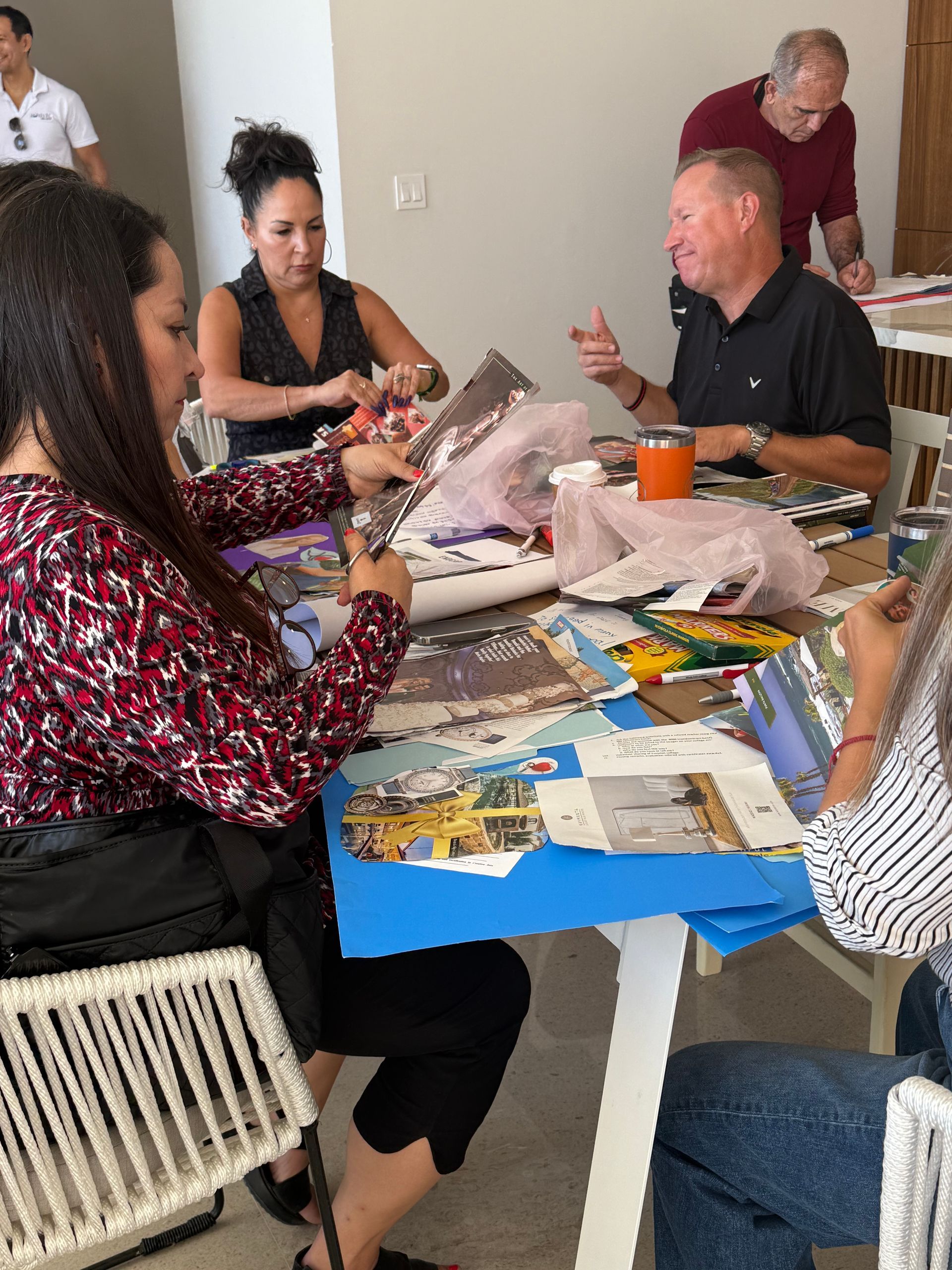 Five people gather around a white table to craft, working with paper, scissors, and foil.