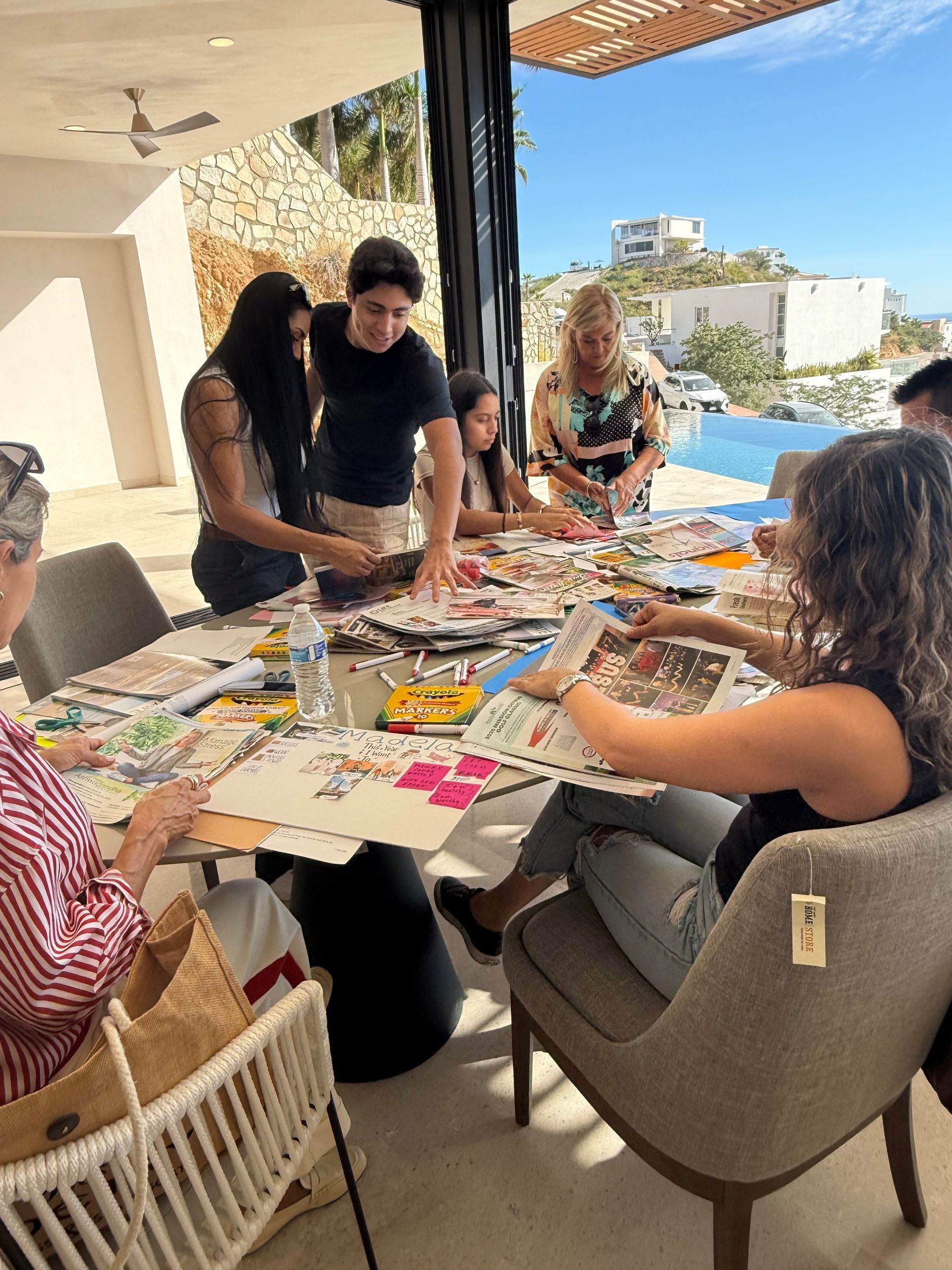 A group gathers around a table on an outdoor patio, working together on a collaborative collage project.