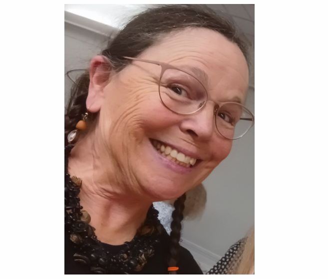 A smiling person wearing glasses and a dark, textured beaded necklace.
