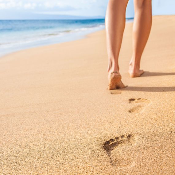 Eine Frau geht am Strand entlang und hinterlässt Fußabdrücke im Sand.