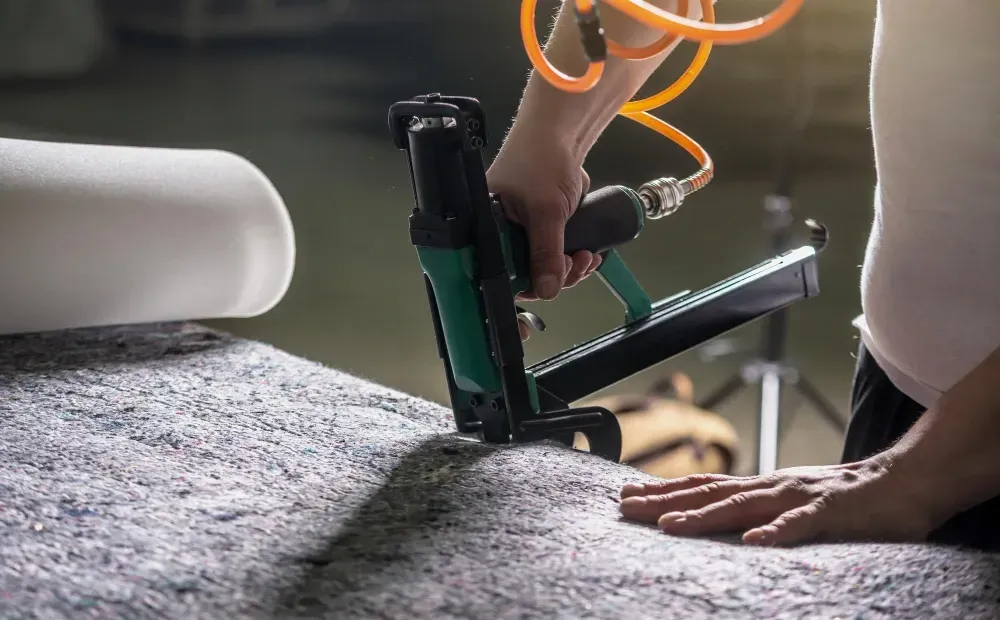 A person is using an air stapler to staple a piece of carpet.