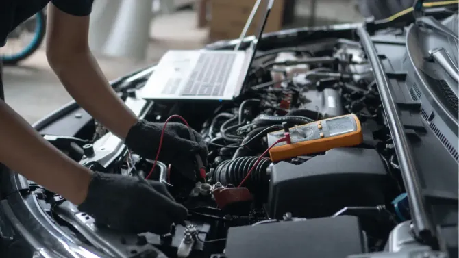 Mechanic testing car battery with a multimeter.