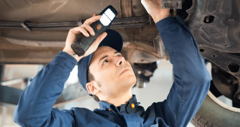 Mechanic inspecting car undercarriage with a work light.