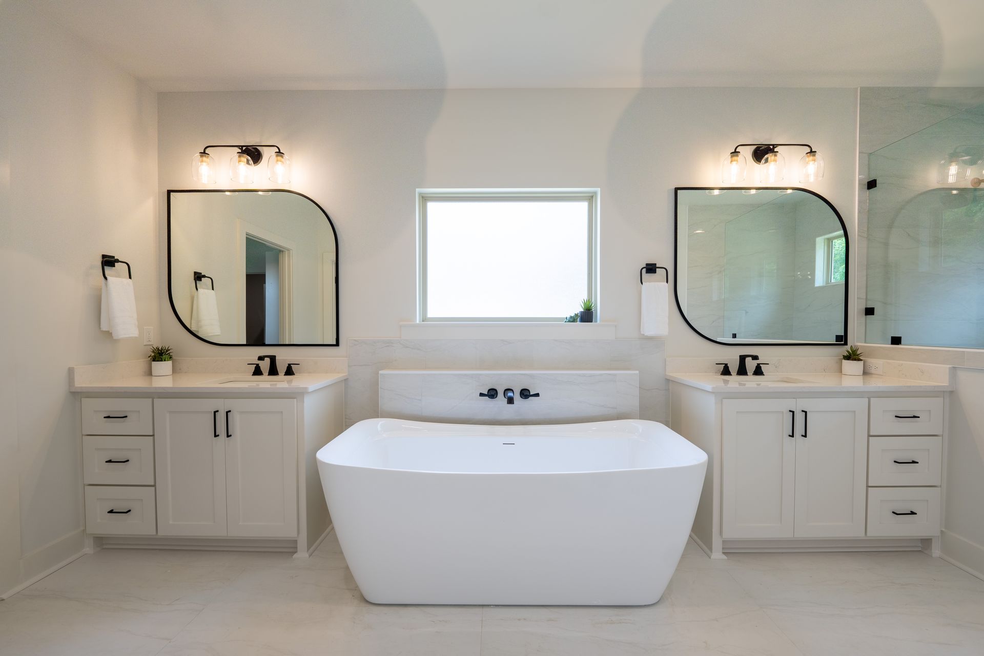 master bath with two vanities and the bath tub in the middle with a big window for natural light