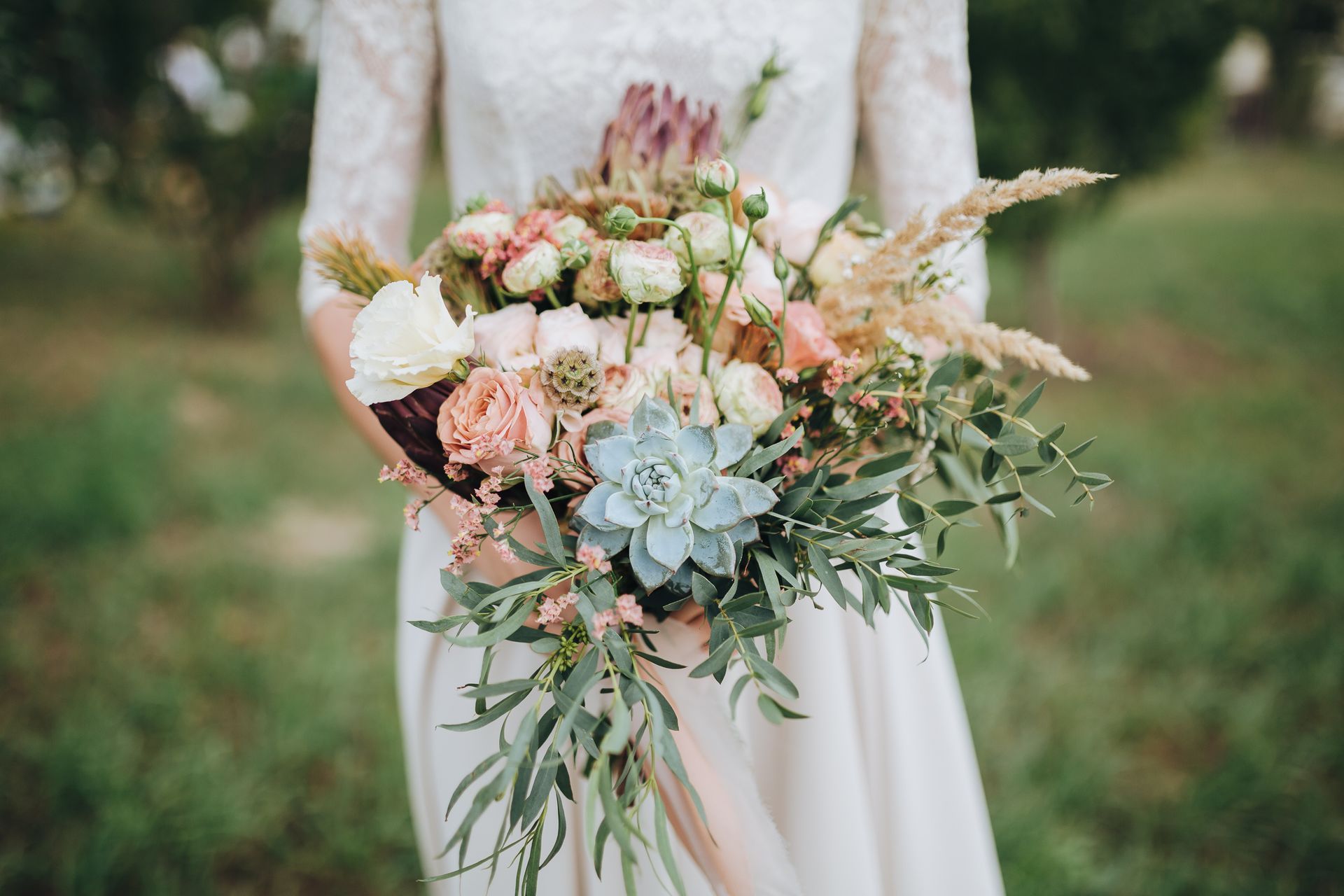 Woman in white dress holding a bouquet of pastel flowers and greenery outdoors.