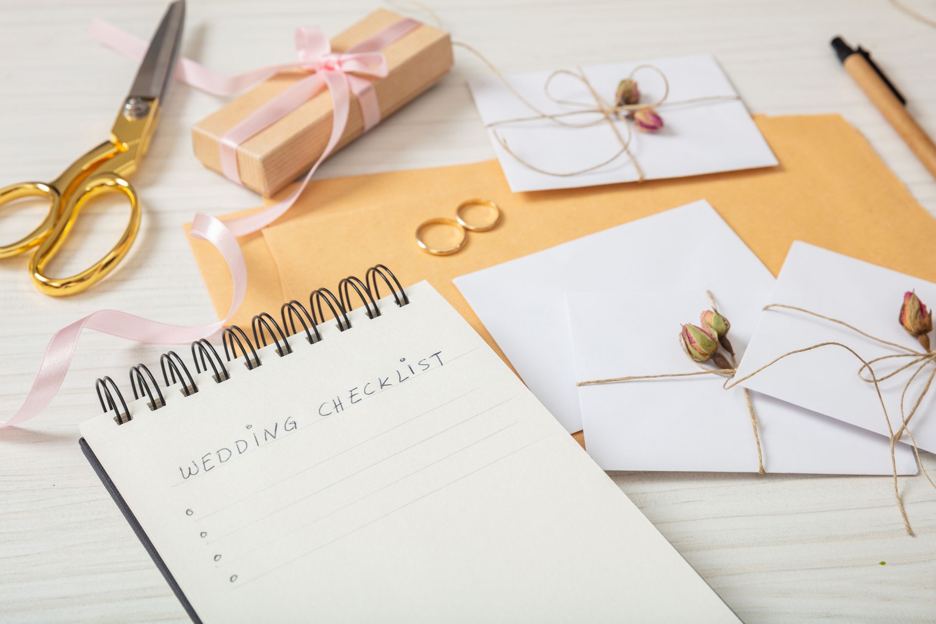 Wedding planning supplies: notebook, invitations, gift box, scissors, rings, pen.