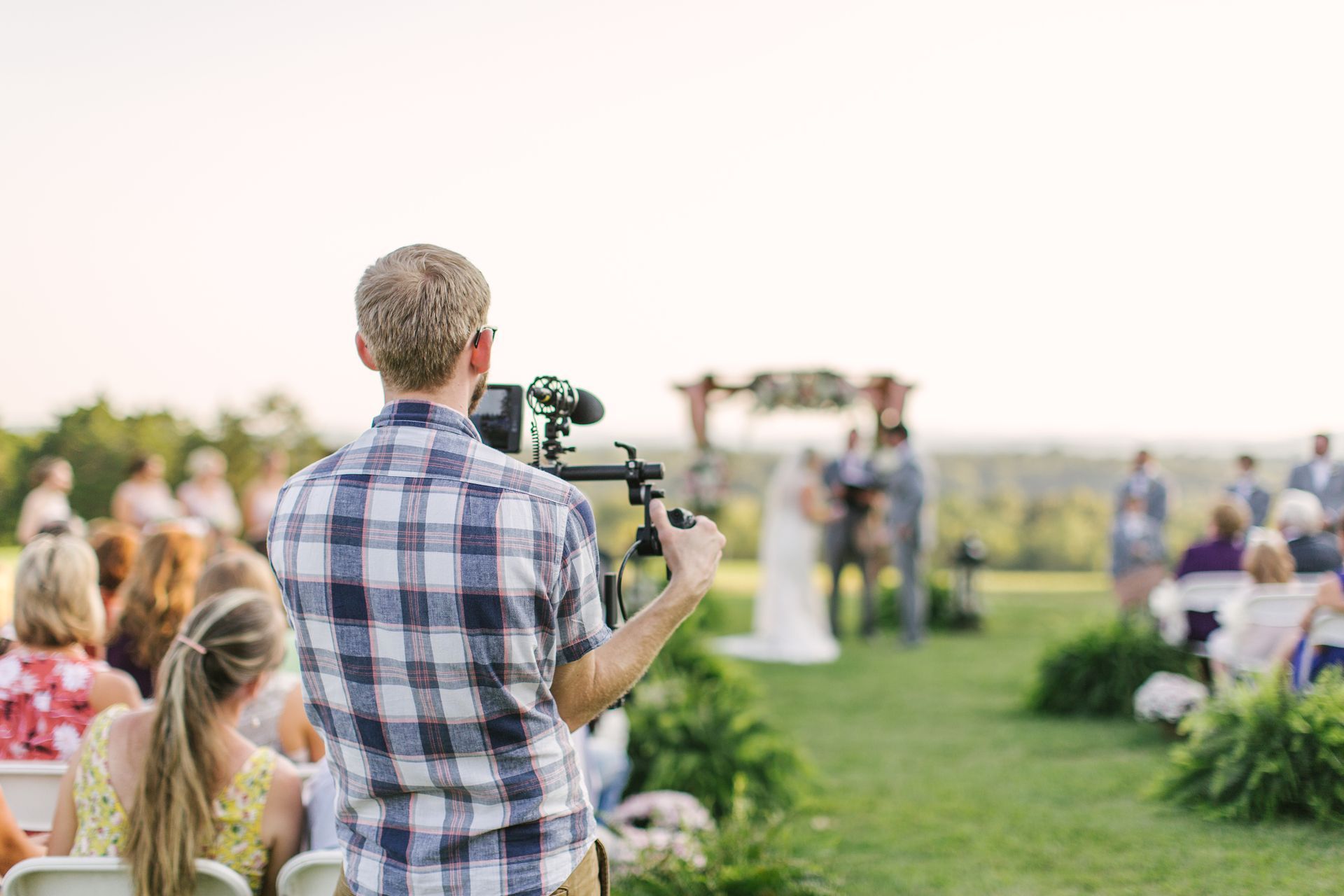 Videographer films a wedding ceremony outdoors on a sunny day.