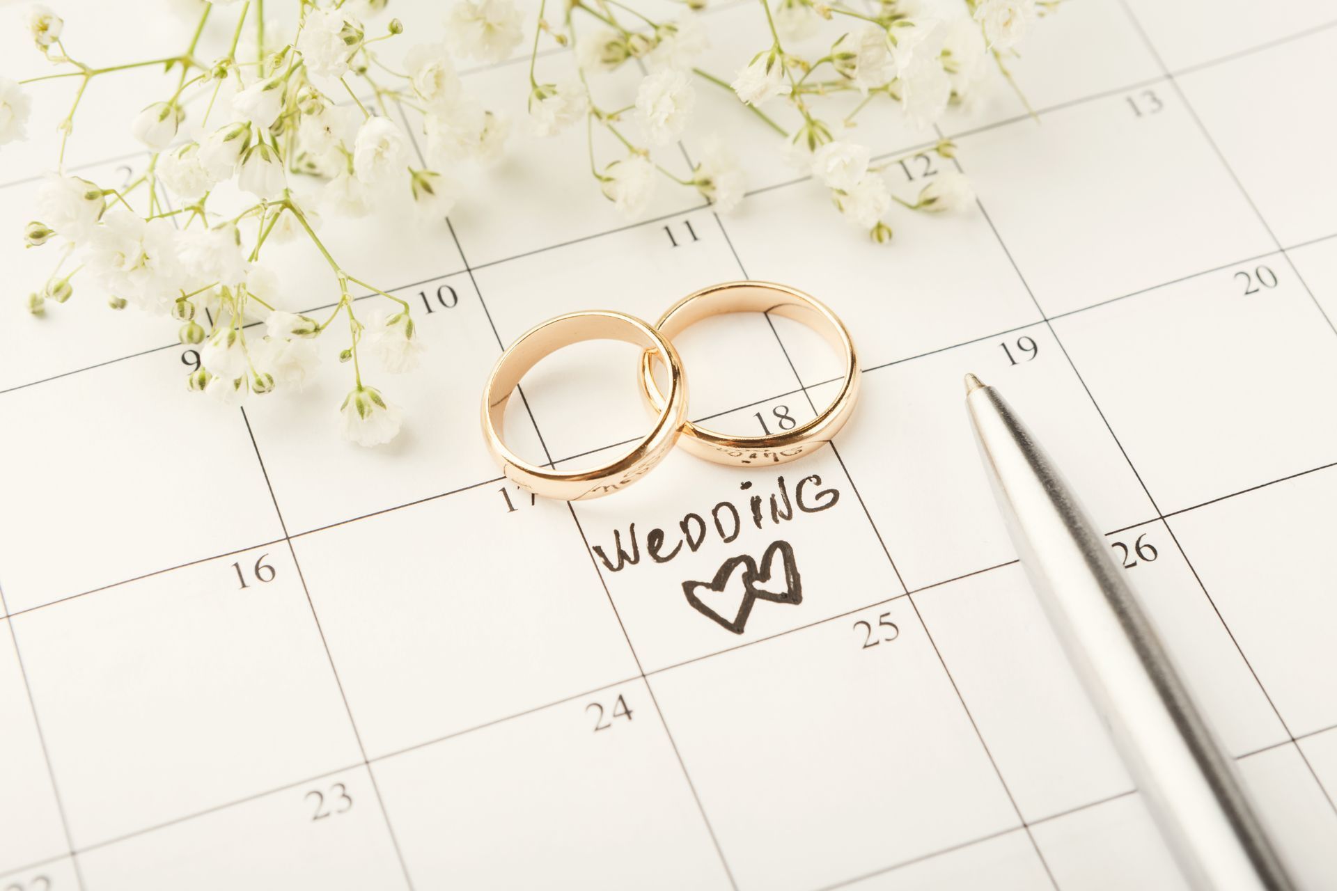 Two gold wedding rings and baby’s breath on a wedding planning timeline calendar.