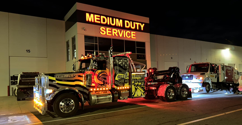 Tow truck at night, towing a smaller truck outside a 