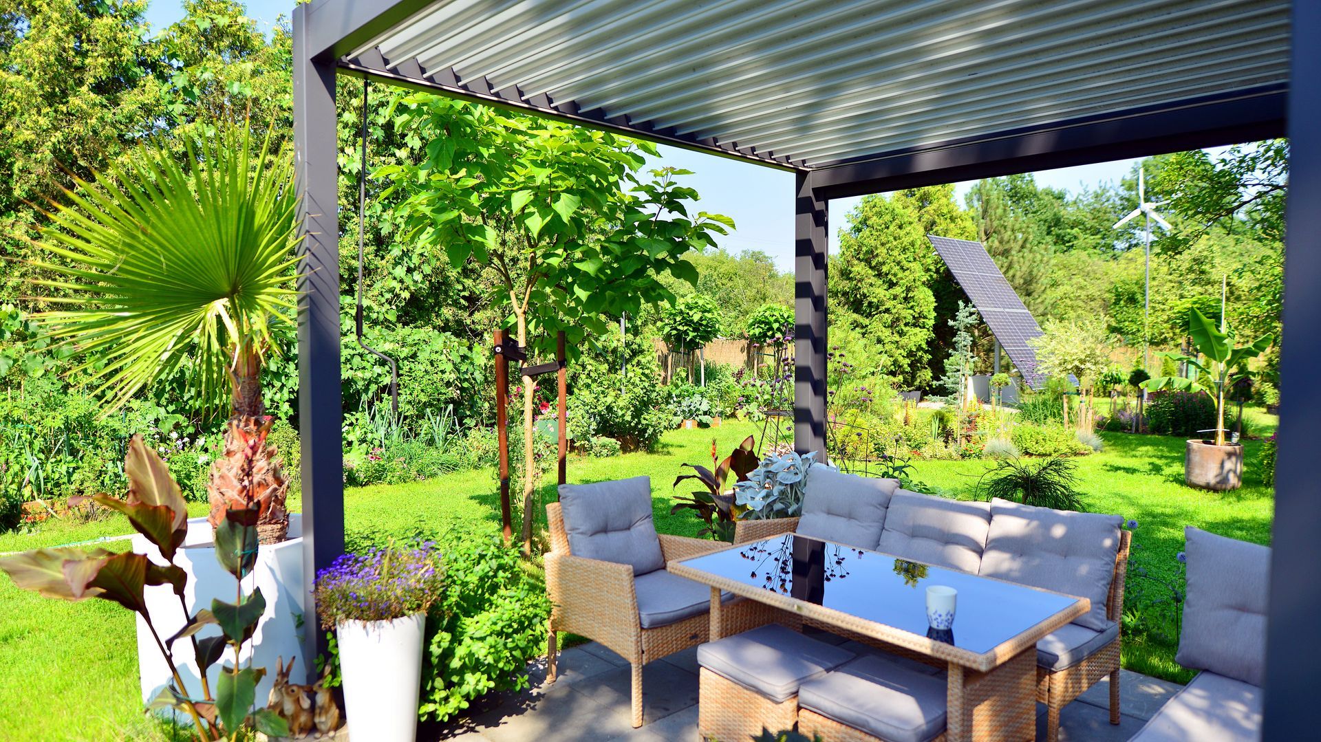 Covered garden patio with wicker seating, coffee table, and lush green tropical plants and trees around it