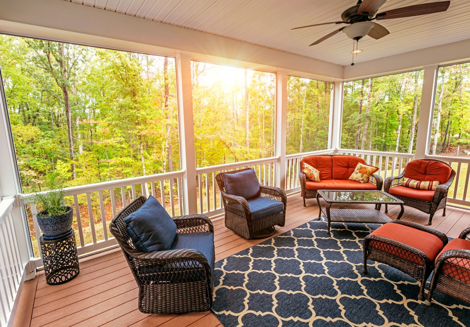 Covered porch with wicker seating, patterned rug, and warm sunset light through screened windows.