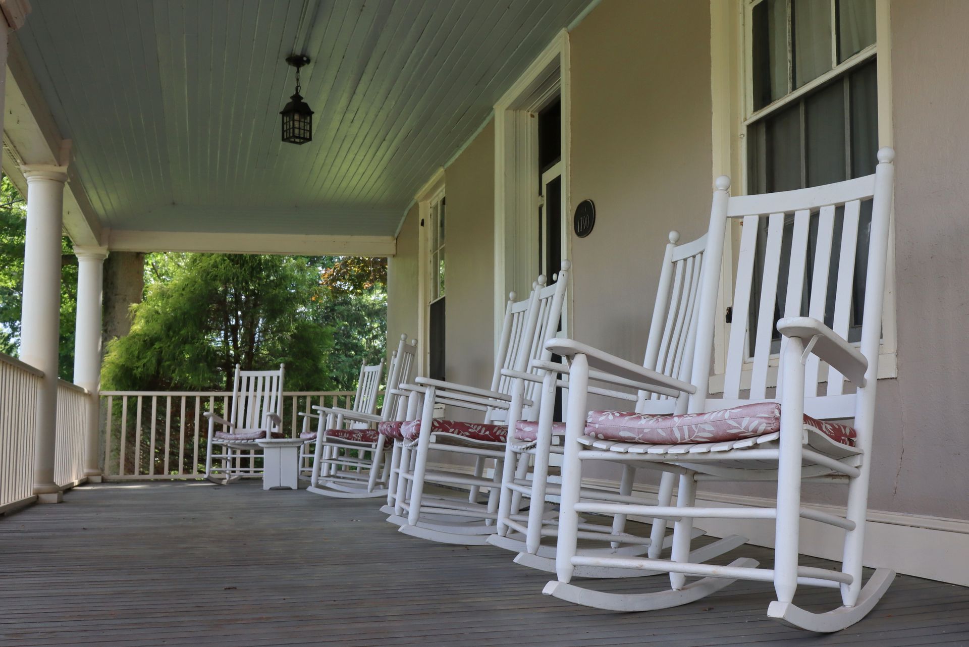 White rocking chairs on a shaded porch with a wooden floor and railing