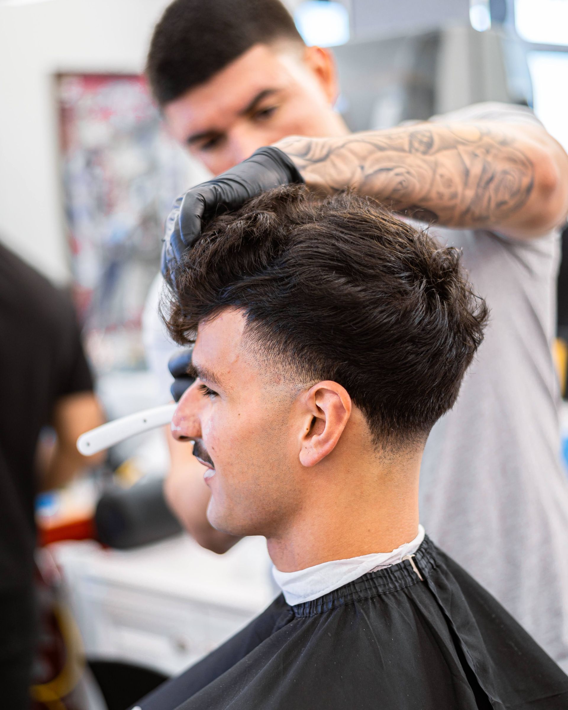 Barber trimming a man's dark hair in a salon, with a black cape and styled fade haircut.