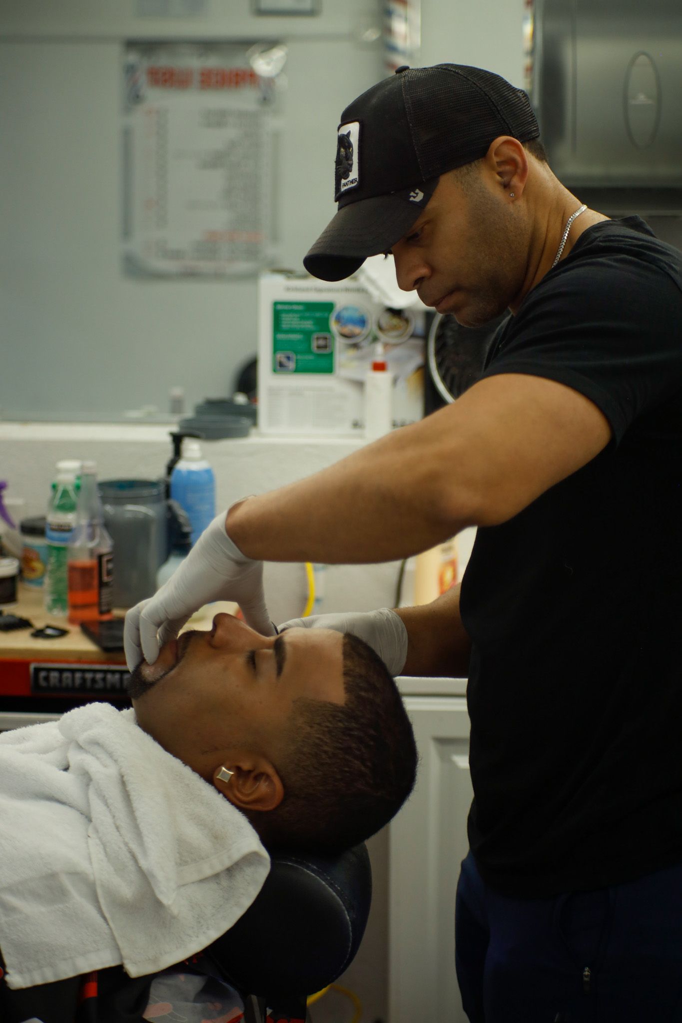 Barber trimming a client’s beard in a shop, with a white towel around the client’s neck.