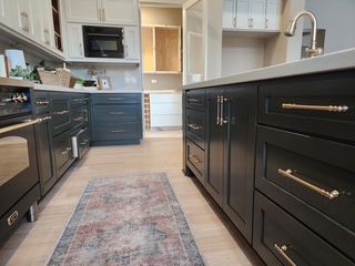 Modern kitchen with dark cabinetry, brass hardware, a patterned rug, and white countertops.