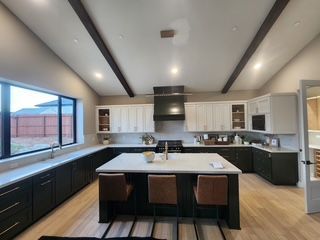 A modern kitchen with dark green lower cabinets, white upper cabinets, a center island with stools, and vaulted ceilings.