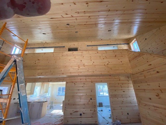 Interior view of a wooden cabin under construction; high ceiling, open loft, ladder, natural wood.