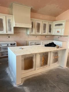 A kitchen under construction with freshly painted white cabinets and a large island, with walls prepped for tiling.