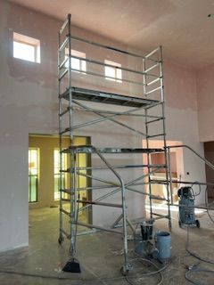 Tall metal scaffolding stands in a room with unfinished, light-pink walls and a concrete floor, next to an air compressor.