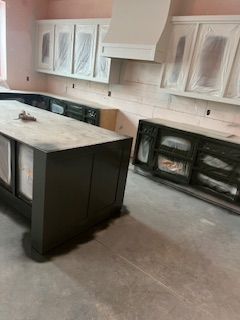 A kitchen under construction featuring a dark island and base cabinets with light upper cabinets and a range hood.