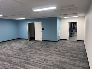 An empty office room with blue walls, gray patterned flooring, and two open doorways leading to adjacent spaces.