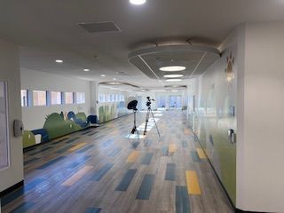 A long hospital hallway with colorful murals, light wood flooring, and a camera tripod set up in the center.