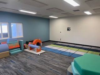 A therapy play room with colorful foam climbing blocks, a floor mat, and a blue accent wall under bright overhead lights.