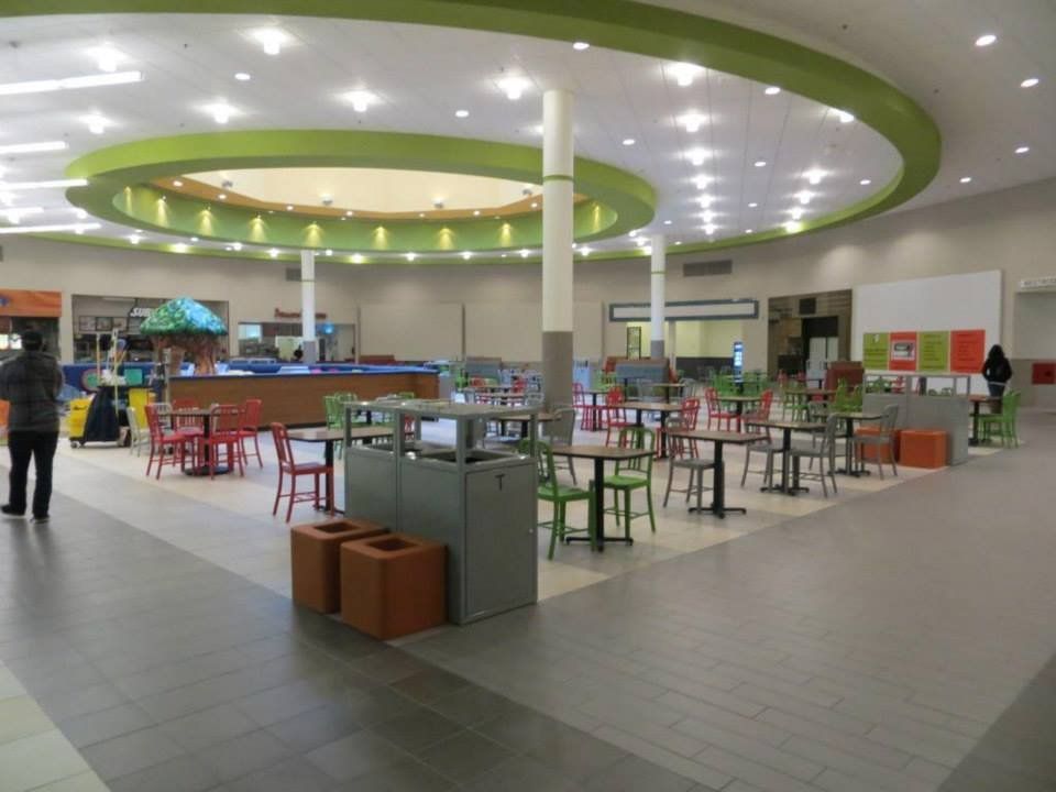 A mall food court with tables and chairs in green and red under a green circular ceiling.