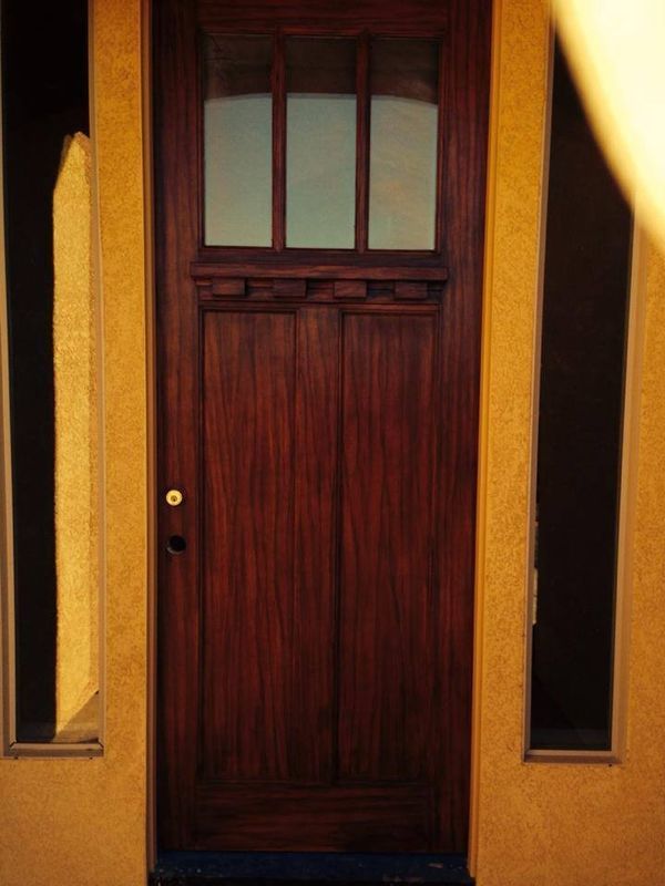 Wooden door with rectangular window panes, flanked by narrow, vertical windows on a gold wall.