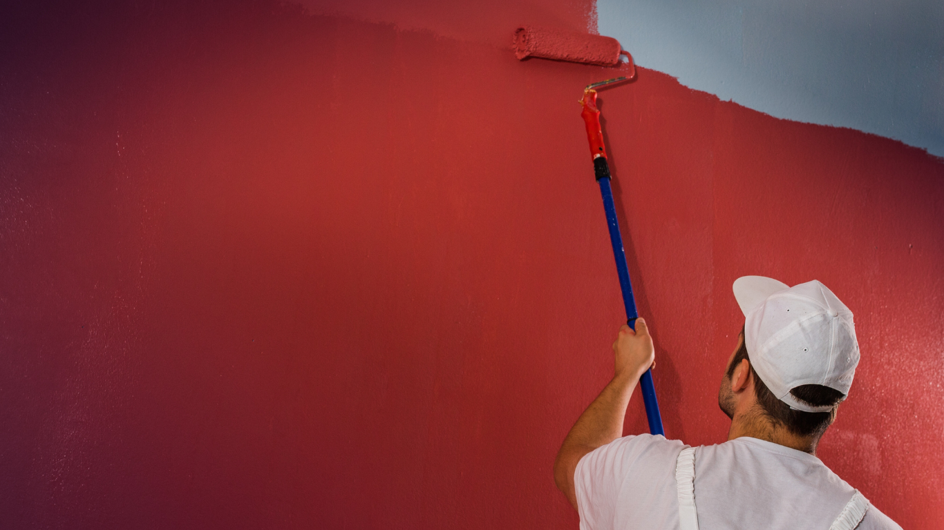 Person painting a wall red with a paint roller.