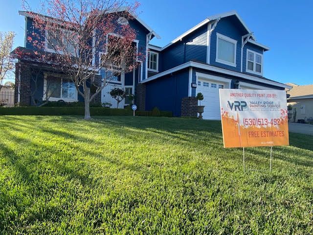Blue house with white trim, green lawn, and a sign in front.