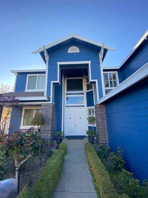 Blue house with white trim, arched entryway, and walkway lined with hedges.