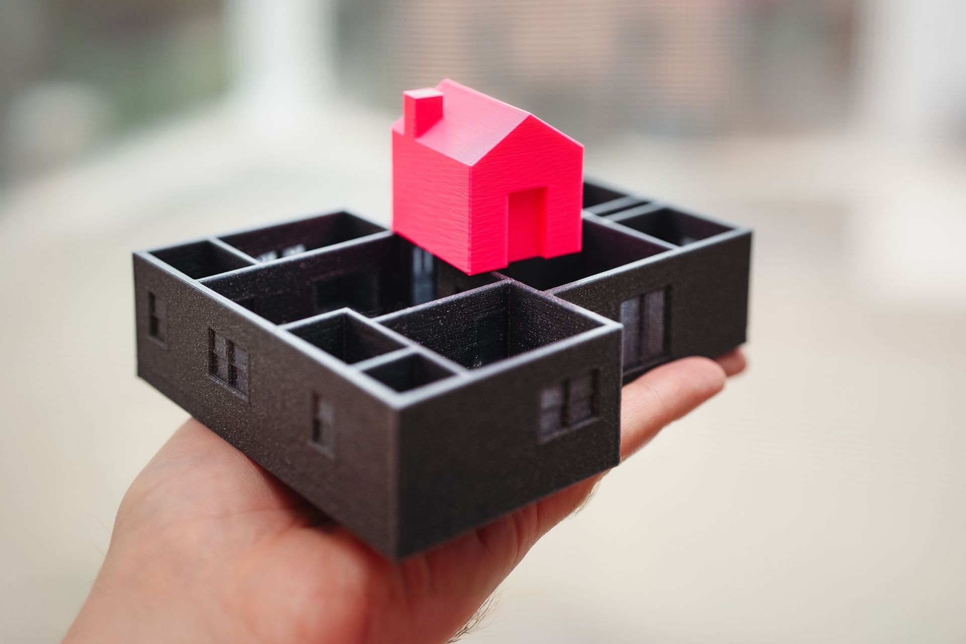 Hand holding a 3D printed architectural scale model of a house with a red roof section