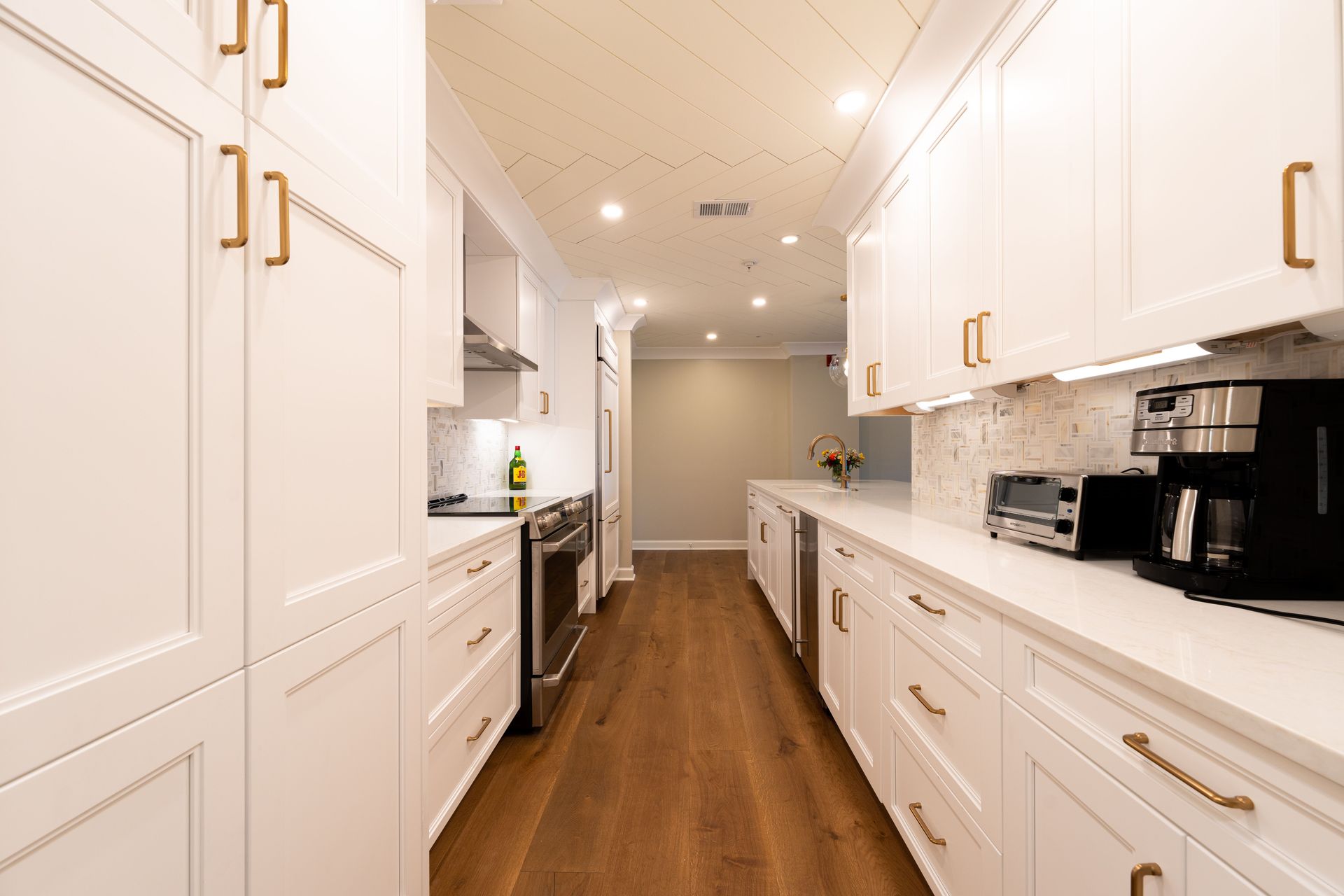 Narrow galley kitchen with white shaker units and wood flooring