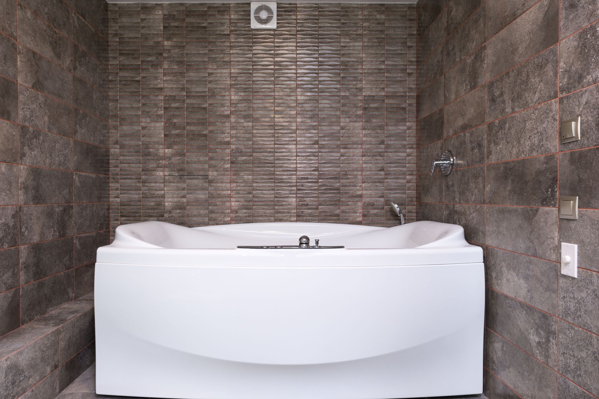 Bath set in an alcove lined with stone-effect mosaic wall tiles