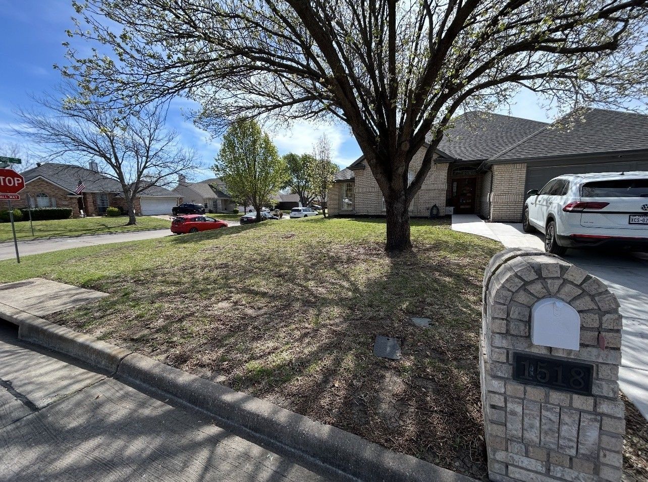 Suburban front yard with a large tree, brick mailbox, and driveway beside a house and parked SUV.