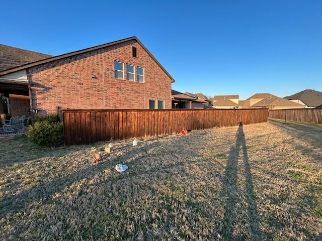 Backyard with red brick house, wooden fence, dry grass, and long shadows at sunset