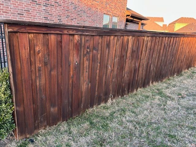 Weathered brown wooden fence beside a brick house, running along a frosty yard.