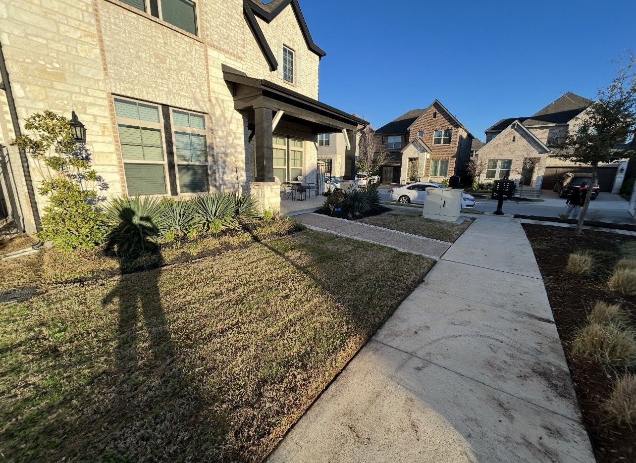 Suburban apartment walkway beside beige homes and landscaped lawns on a sunny day