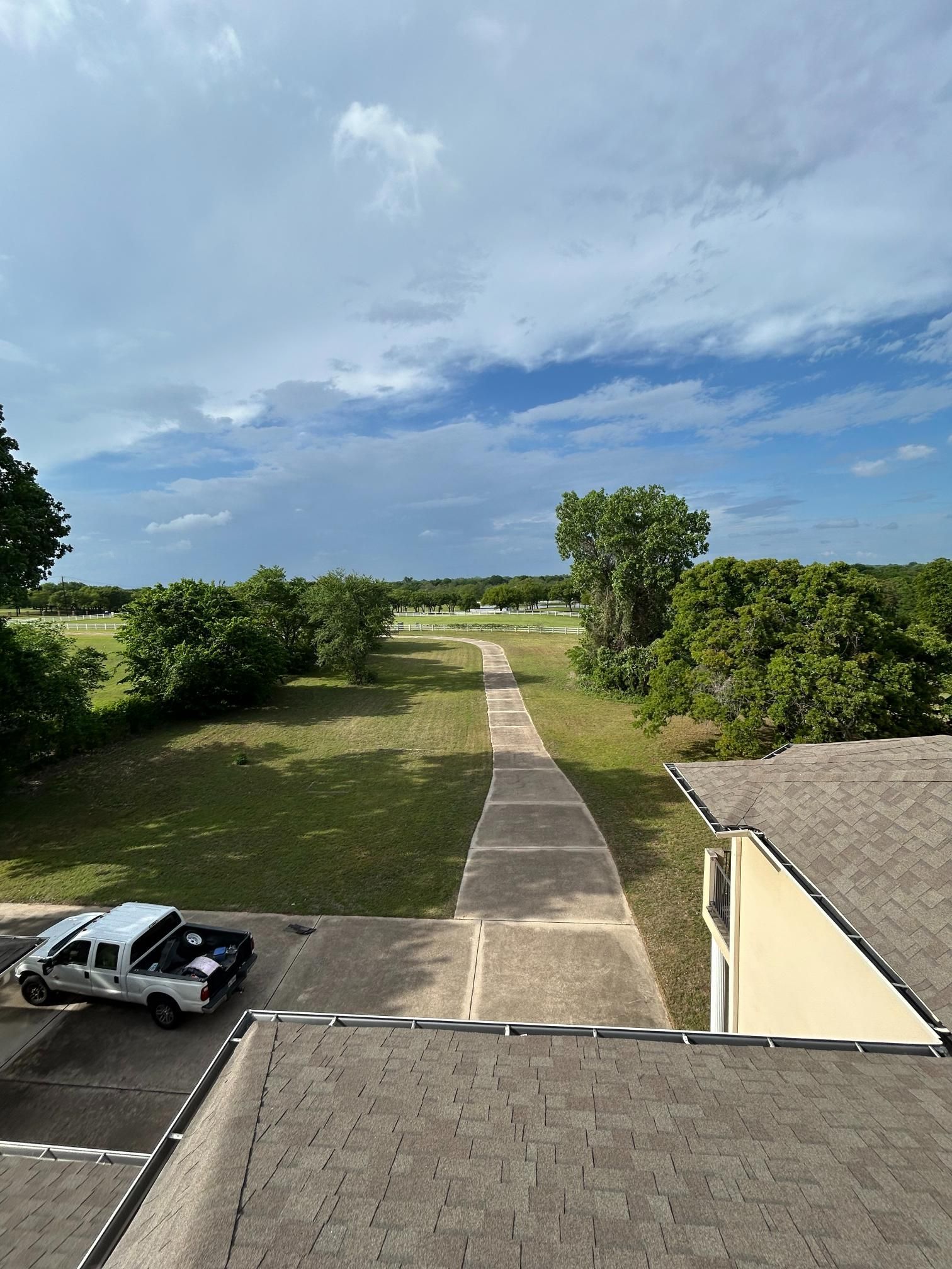 Country driveway and parked car beside a house, leading through a green field under a cloudy sky