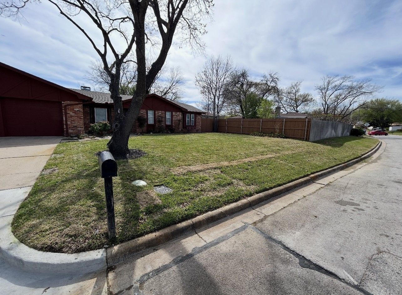 Curved suburban street beside red-brick homes, grassy slope, and leafless trees under a cloudy sky