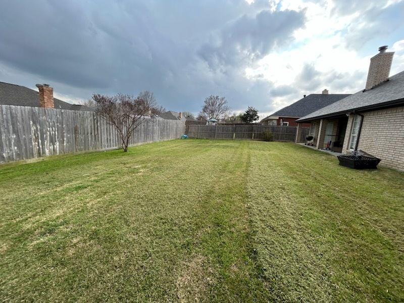 Wide backyard lawn with a wooden fence, cloudy sky, and a house with a covered patio on the right