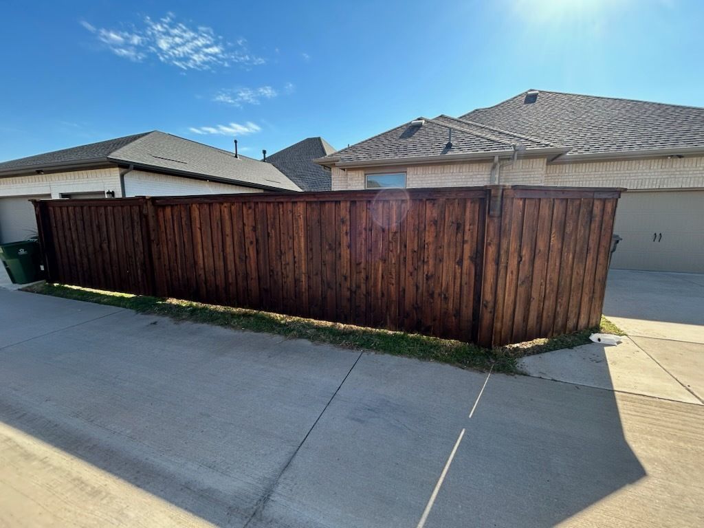 Wooden privacy fence beside a driveway in a suburban neighborhood under a blue sky.