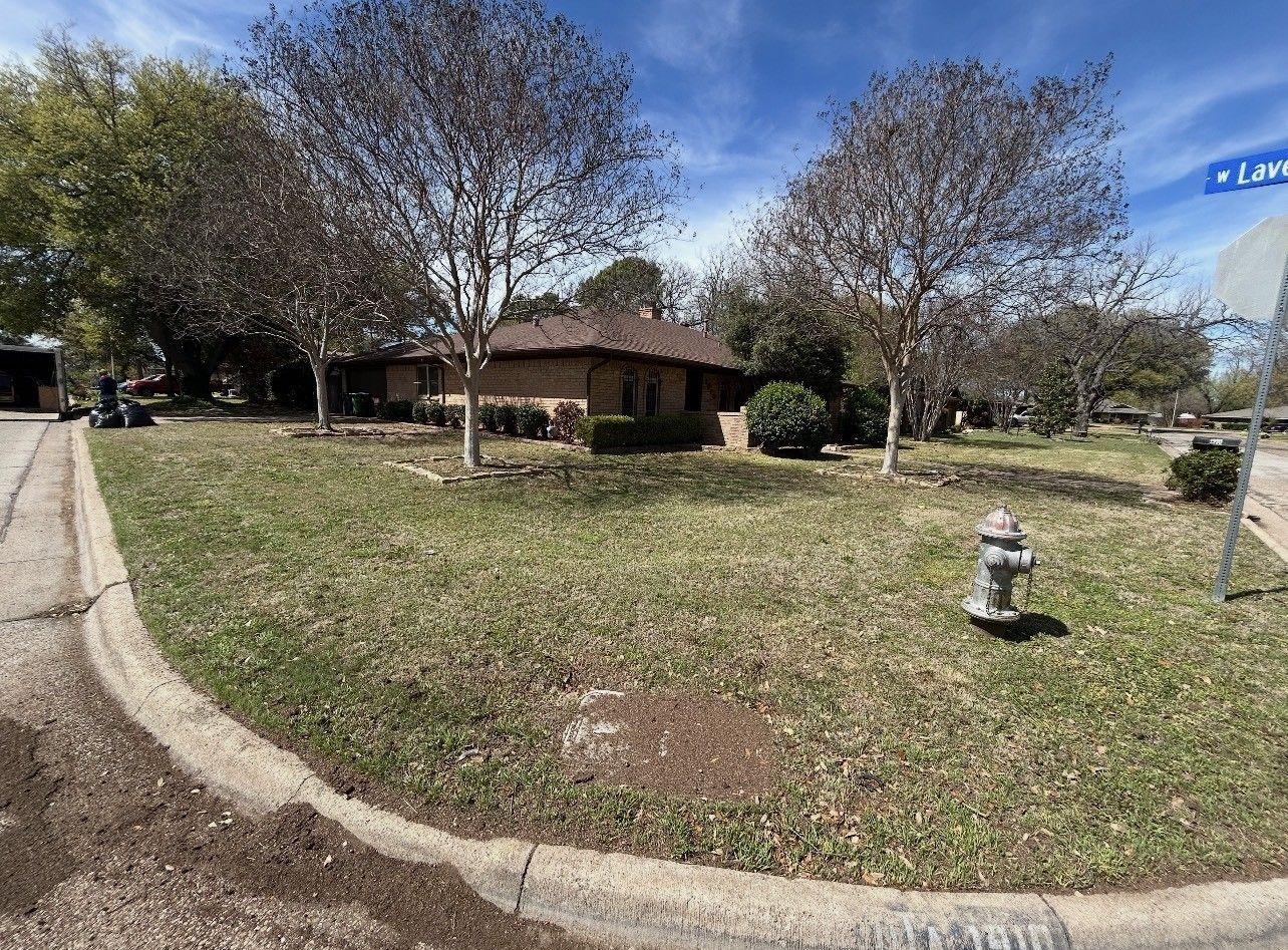 Suburban house with large front lawn, leafless trees, sidewalk, and a fire hydrant under a blue sky