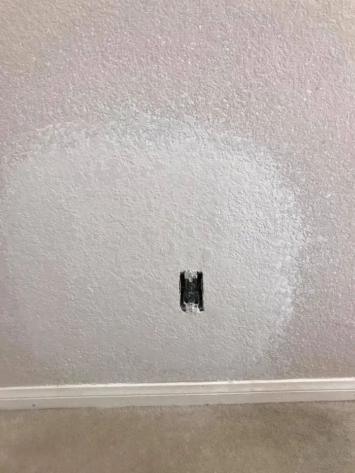 Textured beige wall with a small black electrical outlet opening near the floor.