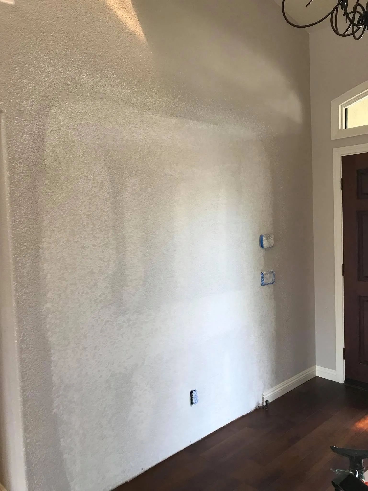 A wall with textured, speckled paint; lower portion is lighter. Dark wood floor and door on the right.