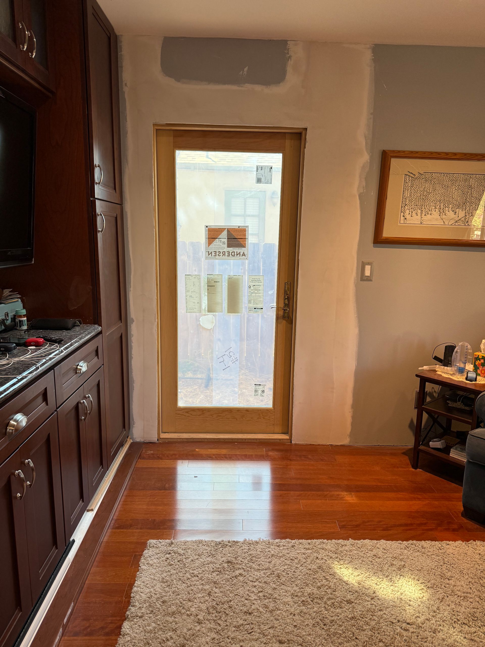 Interior view: a wooden door with frosted glass, flanked by partially finished walls. The floor is hardwood with a rug.
