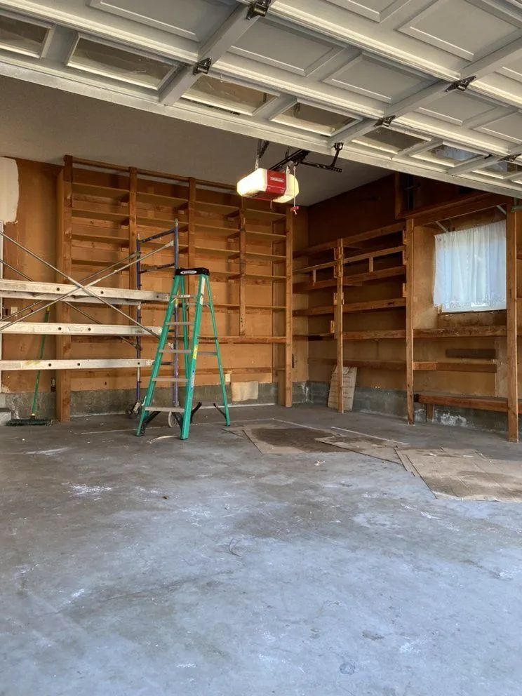 Empty garage with built-in wooden shelves along the walls, a ladder, and a garage door opener.