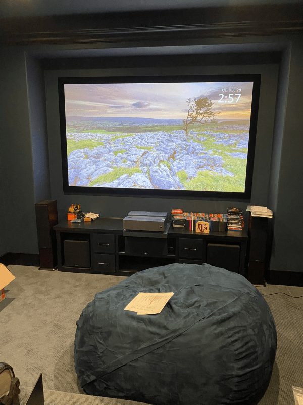 Home theater room with a large TV, black cabinets, and a bean bag chair facing the screen.